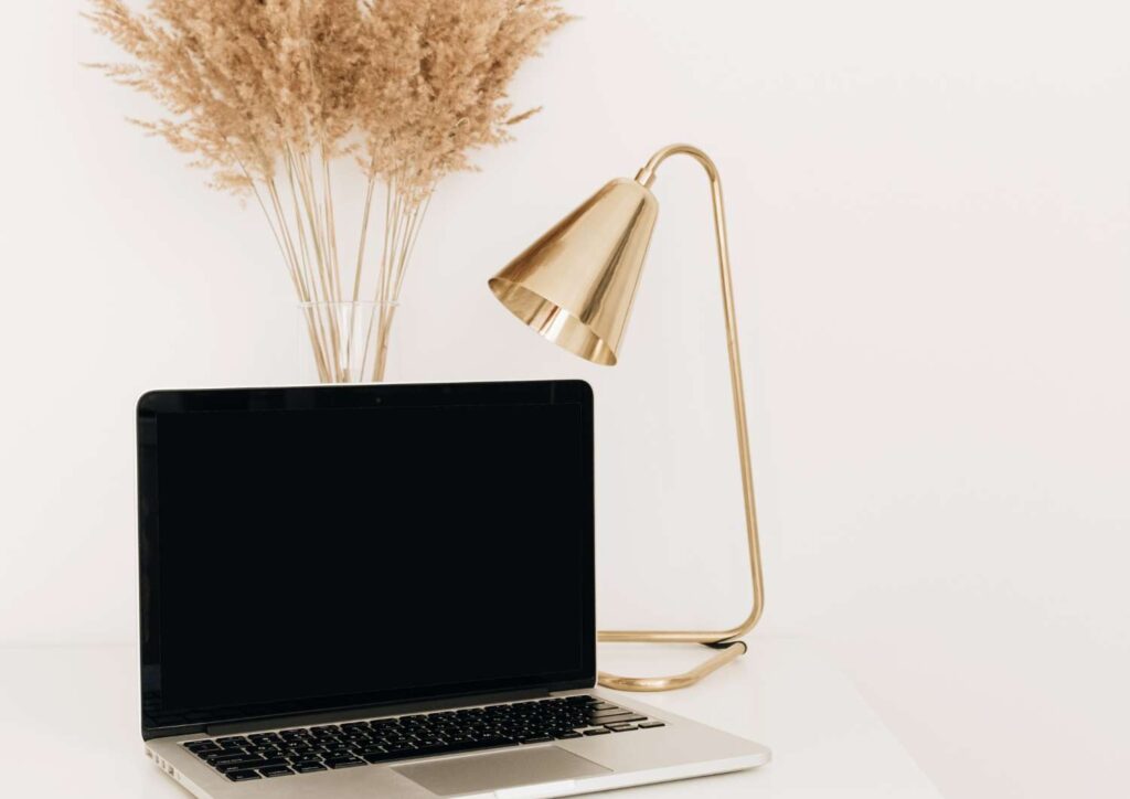 Laptop on desk beside gold lamp and dried flowers, representing calm reflection on financial wellbeing and stress management.