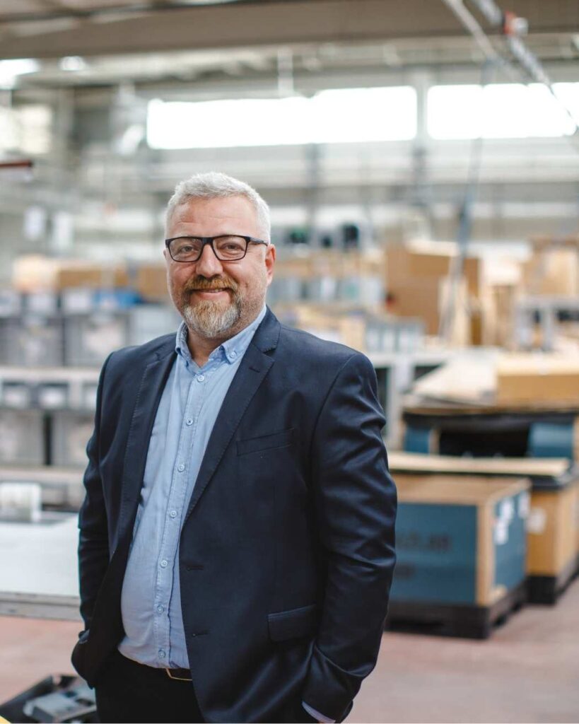 Smiling man in a suit standing in a modern workspace, representing Australians seeking clarity and direction in their finances.